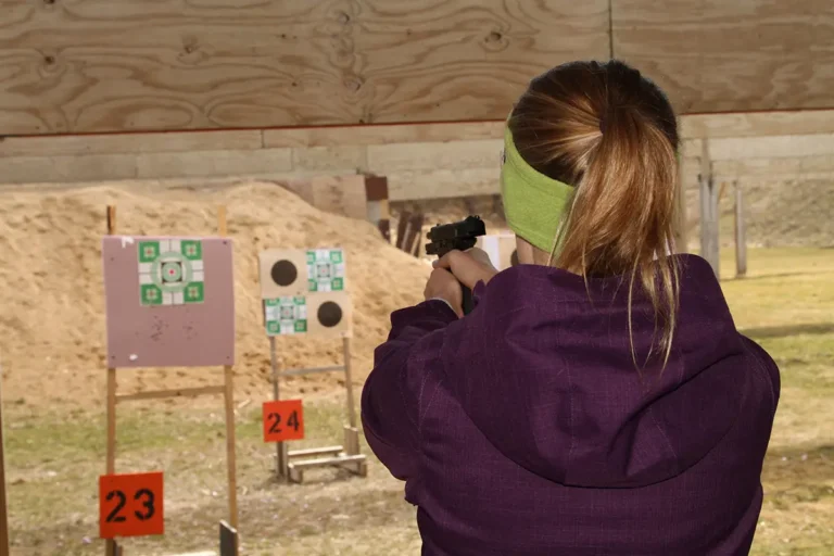 A woman standing with her back to the camera aiming her pistol at targets.